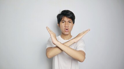 young asian man in white shirt gesturing with crossed arms, saying no or rejecting or blocking