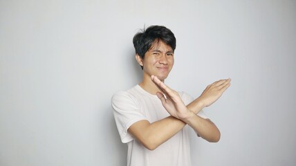 young asian man in white shirt gesturing with crossed arms, saying no or rejecting or blocking