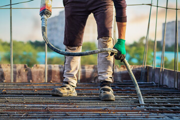 Concrete is compacted by a builder with a concrete vibrator in the hands of a worker at a construction site.