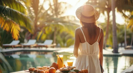Tuinposter A woman in white dress and straw hat stands at the table with food by poolside of luxury hotel resort © Kien