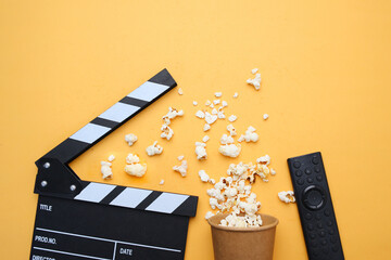 Clapperboard, popcorn and remote control on yellow background