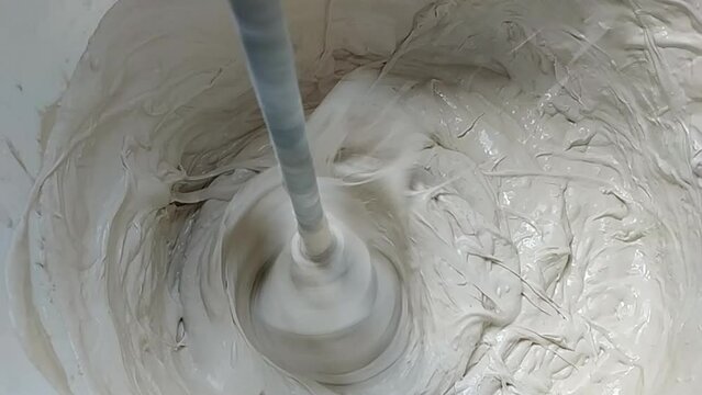 Mixing gypsum putty or white plaster using a electric construction mixer in a plastic bucket. slow motion