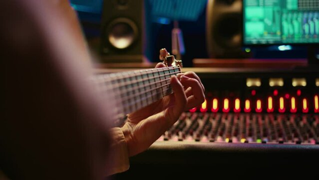 Skilled artist singing on his guitar and recording tunes for a future song, working on new album in control room at studio. Musician composer creating a new track on instrument. Camera B.