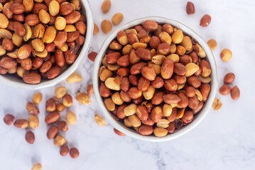 Roasted salted peanuts in white ceramic bowl on white marble background. - Powered by Adobe