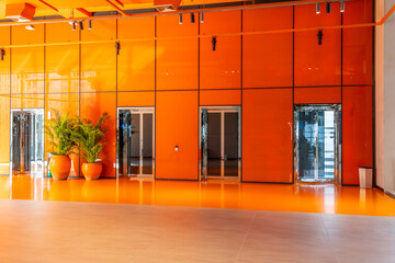 Elevators in orange glossy hall floor with indoor plants