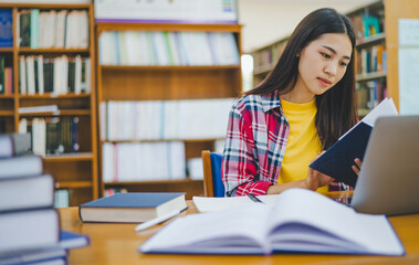 Female college student working on laptop and searching for books to study, make report, find useful information in college room. Concept of reading, learning and intelligence.