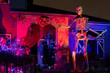 Illuminated night Halloween house outdoor decorations with skeleton and monsters near the house in...