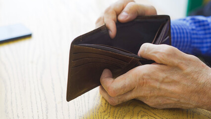 An empty wallet with no money in the hand of an elderly white man about to place an order at a cafe
