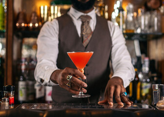 Cutout of a black bartender offering a cocktail served in a martini glass in a traditional cocktail...