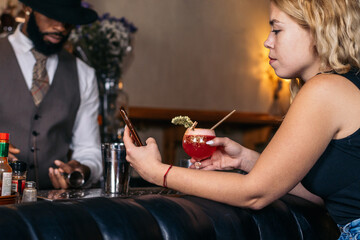 Customer having a cocktail in a traditional cocktail bar while using the smartphone