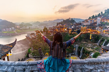 Young female tourist in traditional dress looking at the beautiful landscape at the Furong old Town, The famous tourist destination at Hunan Province, China - obrazy, fototapety, plakaty