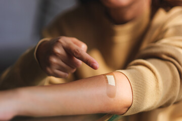 Closeup image of a young woman pointing finger at a adhesive bandage, medical plaster, band aid on her arm - obrazy, fototapety, plakaty