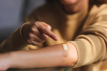 Fotobehang Closeup image of a young woman pointing finger at a adhesive bandage, medical plaster, band aid on her arm © Farknot Architect