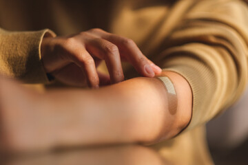 Closeup image of a young woman with a band aid, medical plaster, adhesive bandage on her arm - obrazy, fototapety, plakaty