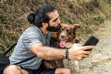adult male mestizo taking a selfie with his border collie dog and kissing its head