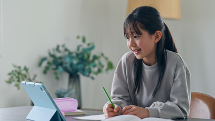 Elementary school girl studying at her desk at home while looking at a tablet PC.