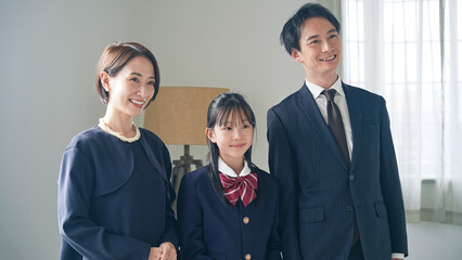 A female student in uniform and her parents in suits take a commemorative photo together. Entrance ceremony. Graduation ceremony.