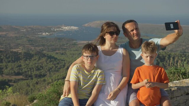 Young family with kids making a selfie with mobile phone on top of El Toro mountain in Menorca, Spain