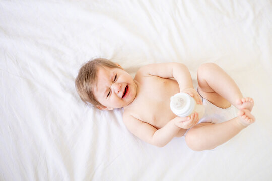 crying baby a newborn girl in a diaper lies on a white crib in a bright bedroom and sucks a pacifier or a bottle of milk, a place for text, close-up