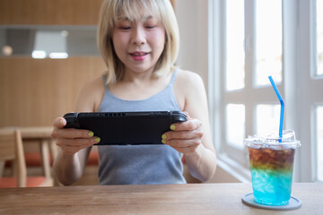 Asian woman playing video game on a portable gaming console at cafe.