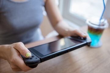 Asian woman playing video game on a portable gaming console at cafe.