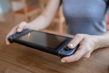 Asian woman playing video game on a portable gaming console at cafe.