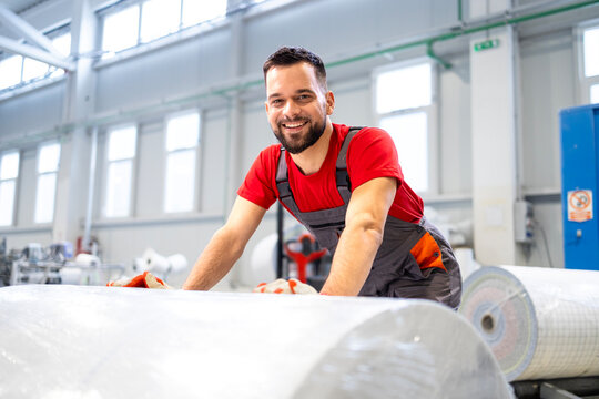 Factory worker pushing large rolls of paper.