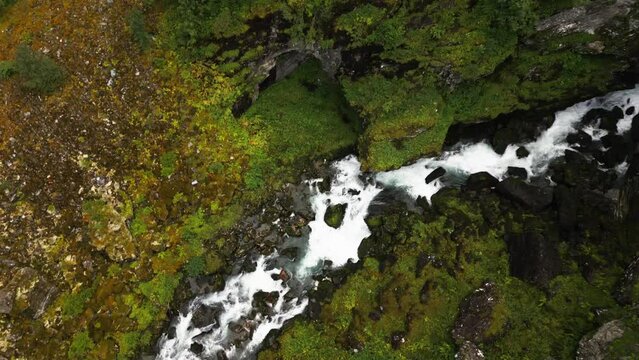 waterfall and river through forest in a mountain range from above, norway, europe, drone