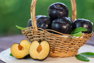 Fresh Black Plum fruit in Bamboo basket on wooden table in garden, Fresh Black Plum with slices on blurred greenery background.