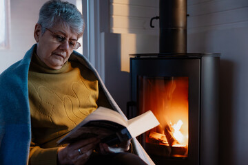 Reading a book by the fireplace. The grandmother is sitting by the warm fireplace with a book in...