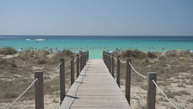 Wooden path over the sandy beach to the turquoise sea of Son Bou in Menorca, Spain