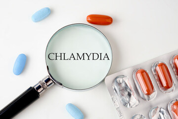 Medical concept. Word Chlamydia. through a magnifying glass on a white background next to pills,...