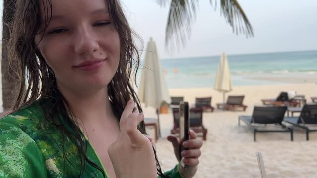 A girl with great delight drinks a coffee drink on beach shows her fingers just perfect Okay she shows radiates the joy of life pleasure from relaxing in a green pareo with wet hair. after swimming