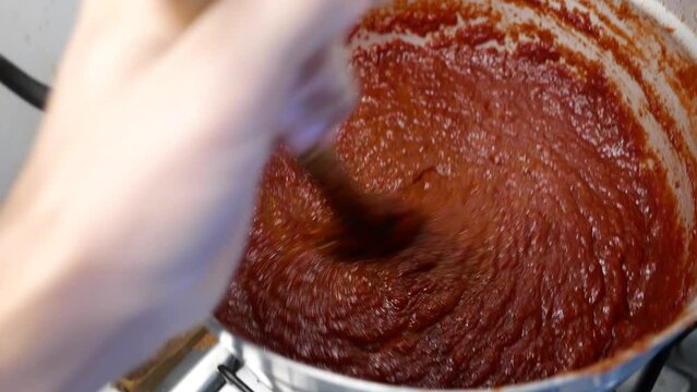 POV: person mixing fruit jam in a big pot. Person making guava jelly. A big guava jam pan (Psidium guajava). Guava jelly on the stove. Guava jelly pot close-up shot, POV angle. Candy recipe. 