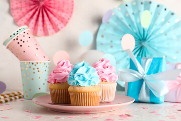 Delicious cupcakes with gift boxes and decorations on table against white grunge background. Gender...