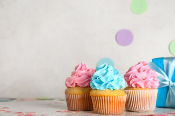 Delicious cupcakes with gift box and decorations on table against white grunge background. Gender...