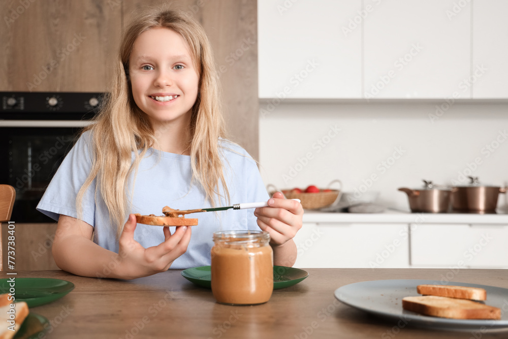 Wall mural little girl making toast with peanut butter in kitchen