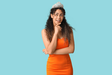 Thoughtful young African-American woman in stylish orange prom dress and tiara on blue background © Pixel-Shot