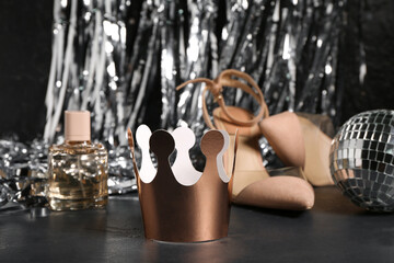 Paper crown with stylish high heels, disco ball, bottle of perfume and tinsel on black background....