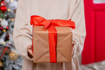 Close-up of a gift in the hands of a young woman, against the backdrop of Christmas decorations....