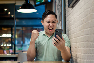 Asian man Engaging with Smartphone in a Modern Cafe Setting. Looking to good news on his phone...