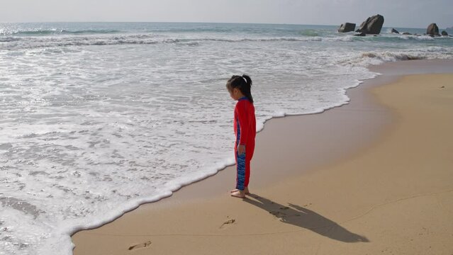 little asian girl playing on the beach, curious looking chasing wave