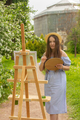 Beautiful female artist painting on canvas and wooden easel in spring botanical garden. Art process of woman outdoor