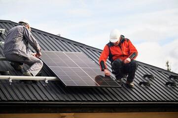 Mounters installing photovoltaic solar panels on roof of house. Men engineers in helmets building...