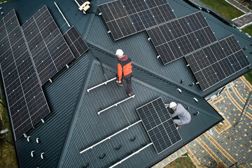 Workers building photovoltaic solar module station on roof of house. Men electricians in helmets...