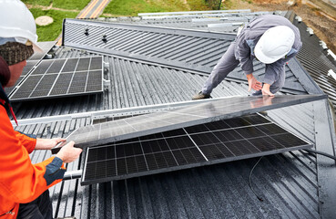 Workers building solar panel system on roof of house. Men technicians in helmets carrying...