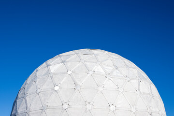 Abandoned dome of an old Soviet military radar from the Cold War. A huge structure in the form of a white sphere against a blue sky. The surface of a sphere of triangles.