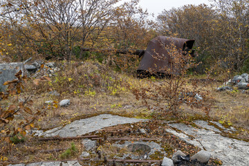 Old abandoned artillery gun in the forest. Rusty broken cannon. Ruins of a mid-20th century Soviet defensive artillery battery on the coast of the Sea of Okhotsk. Magadan region, Far East of Russia.