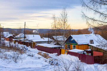 Winter rural landscape. View of a snow-covered street and wooden houses. Firewood lies in the snow near the houses. Cold weather. Winter. Tynda, Amur region, Siberia, Russia.