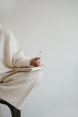 Woman in white wearing write or draw in notebook sitting over white wall. Artist, writer work process concept. Neutral beige color